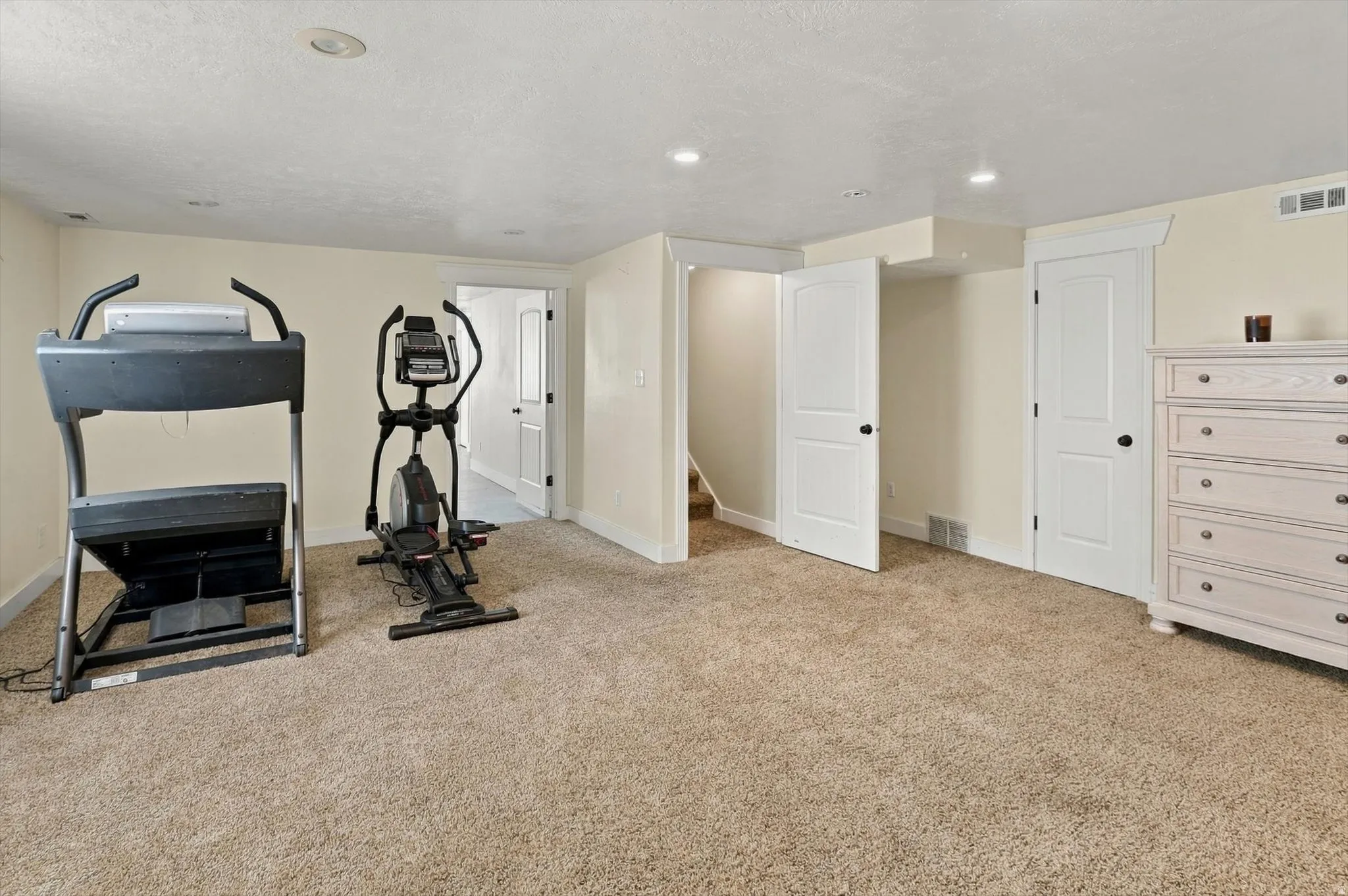 Carpeted recreation room with recessed lighting, multiple white paneled doors, and painted walls