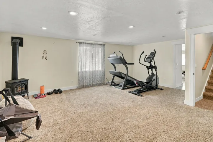 Carpeted room featuring a wood-burning stove, recessed lighting, and a window with curtains
