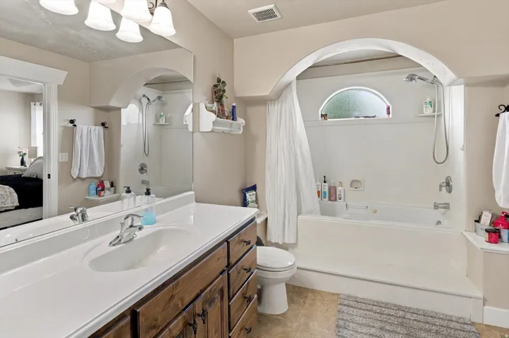 Bathroom featuring a wood-finish vanity with an integrated sink, a large wall-mounted mirror, white bathtub with shower combination, and an arched alcove