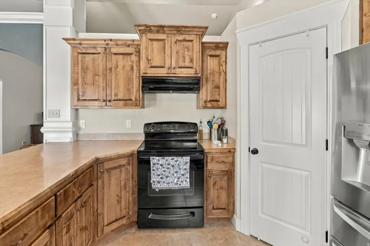 Kitchen featuring wood-finish cabinetry, solid surface countertops, a black electric range, and a matching black range hood