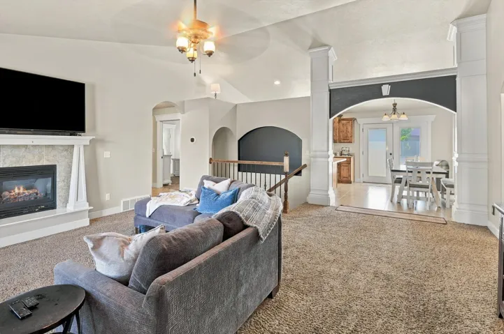 Living area featuring a textured fireplace surround, white mantel, vaulted ceiling, and ceiling fan