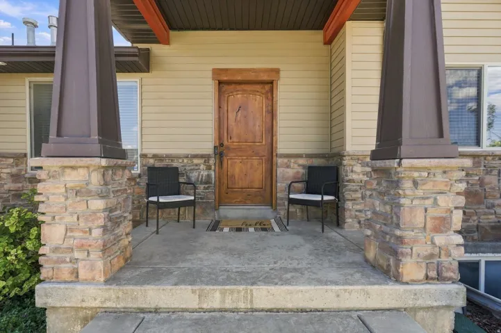 Wood-finish paneled entry door with a wood-trimmed frame, stone veneer detailing, siding exterior, and substantial porch columns