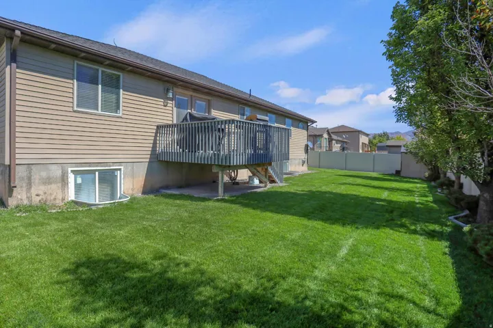 Expansive backyard featuring a manicured lawn, a two-story residence with tan siding, and a wood deck with railings