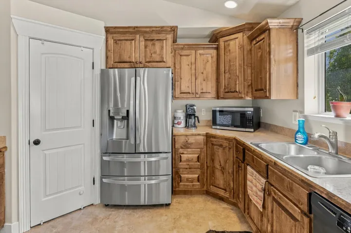 Wood-finish cabinetry, stainless steel French door refrigerator, dual basin stainless steel sink, and light-toned countertops