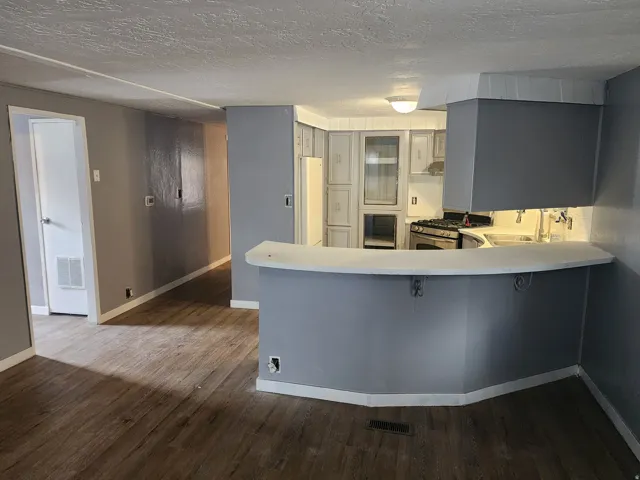 Kitchen featuring a gas range, curved breakfast bar, under-cabinet lighting, and white cabinetry