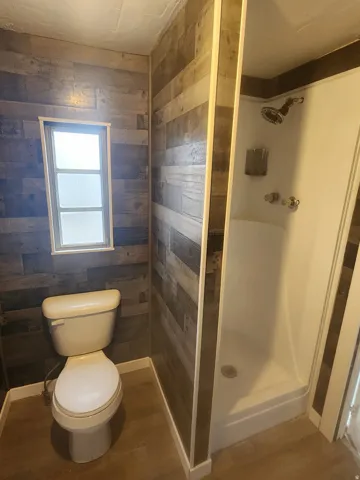 Bathroom featuring wood-finish accent walls, a white toilet, and a stand-up shower with a chrome showerhead