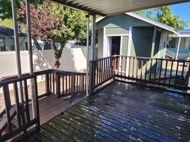 Covered deck with dark wood-finish railing, partially visible privacy fencing, and a detached structure