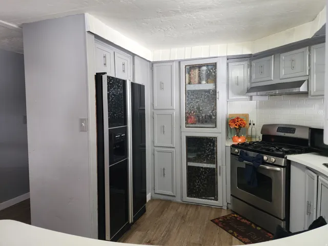 Kitchen featuring wood-finish flooring, white subway tile backsplash, stainless steel range with overhead ventilation, and light gray cabinetry