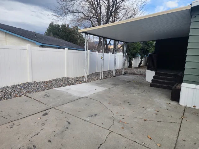 Concrete driveway with an attached carport, leading to a raised entry deck with steps and a handrail