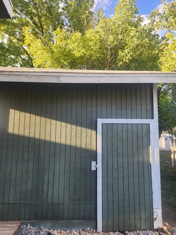 Vertical panel siding with a contrasting white trim, featuring a side gate and a gravel border