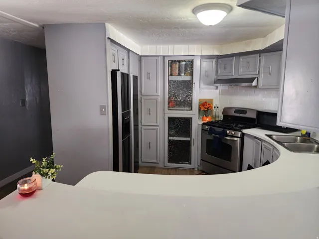 Kitchen featuring light gray cabinetry, stainless steel appliances, a white subway tile backsplash, and wood-finish flooring