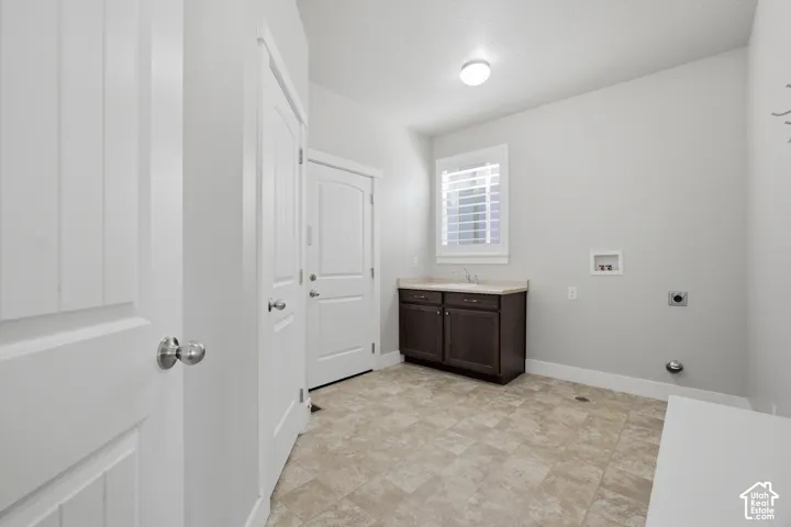 Utility room featuring tile flooring, a window with plantation shutters, a built-in sink with dark wood cabinetry and light-colored countertop, and a ceiling-mounted light fixture