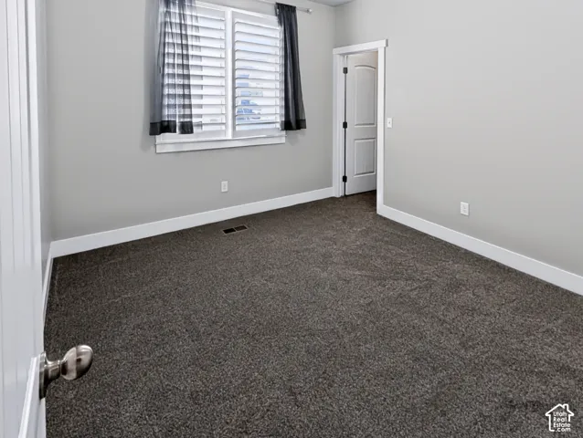 Neutral gray wall color, dark gray carpet flooring, white trim, white interior doors, and window with white plantation shutters