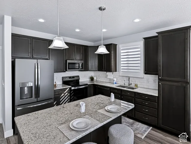 Kitchen featuring dark wood-finish cabinetry, stainless steel appliances, a white subway tile backsplash, light-toned countertops, and an island with pendant lighting