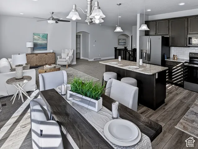 Spacious open-concept layout with wood-finish flooring, a kitchen island featuring a light-toned countertop, dark cabinetry, and white subway tile backsplash