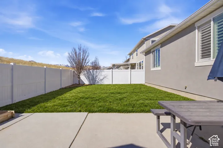 Expansive concrete patio with a manicured lawn, perimeter fencing, and mature landscaping