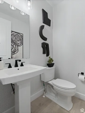 Pedestal sink with matte black fixtures, contemporary wall-mounted lighting, patterned wallpaper, and wood-finish flooring
