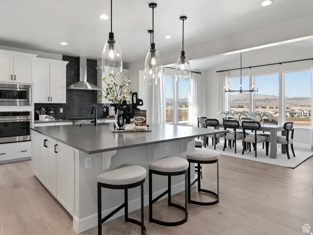 Open-concept kitchen and dining area featuring white cabinetry, a large kitchen island with countertop seating, stainless steel appliances, and wood-finish flooring