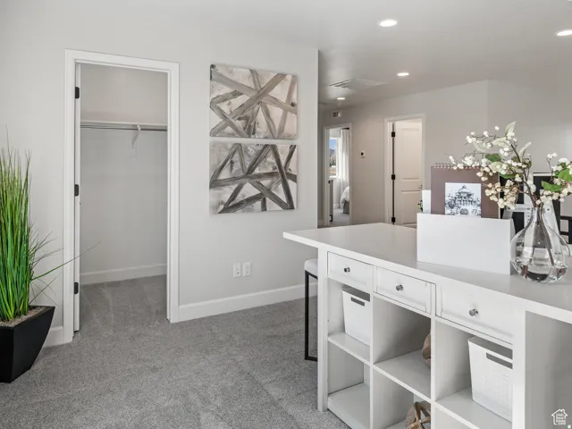 Plush carpet flooring, recessed lighting, white built-in storage unit with drawers and open shelving, and a walk-in closet with shelving