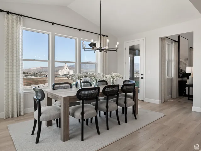 Vaulted ceilings with a contemporary chandelier, multiple large windows, a glass-paneled door, and light wood-finish flooring