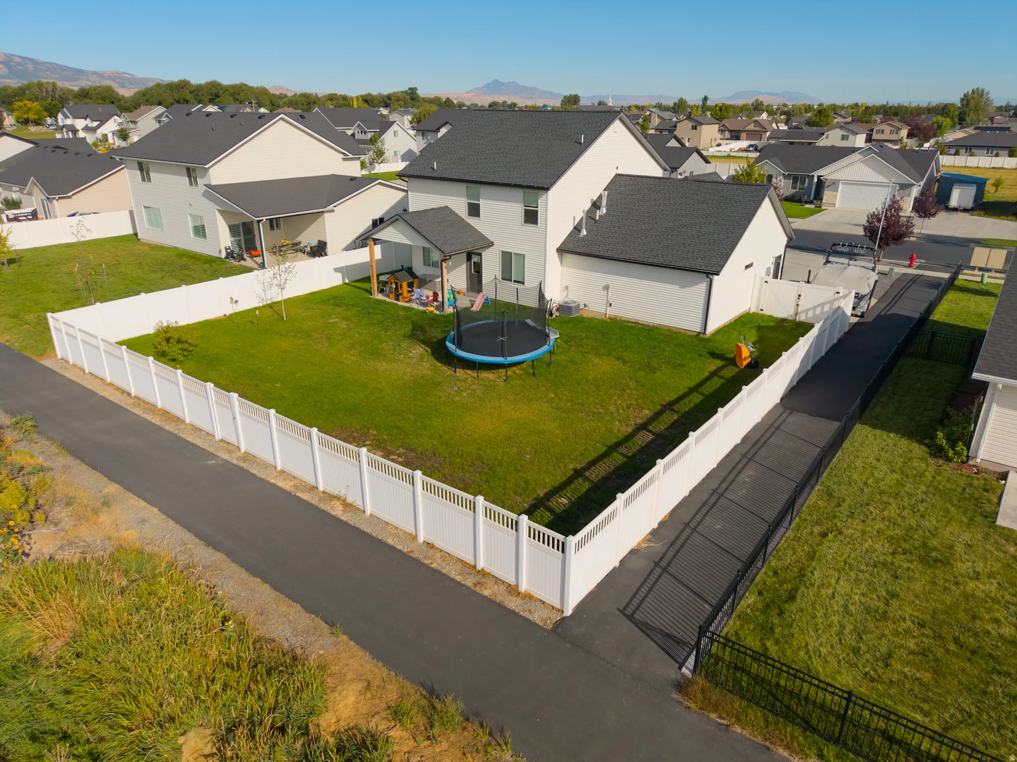 Expansive green lawn enclosed by white fencing, featuring a covered patio and an additional uncovered patio area