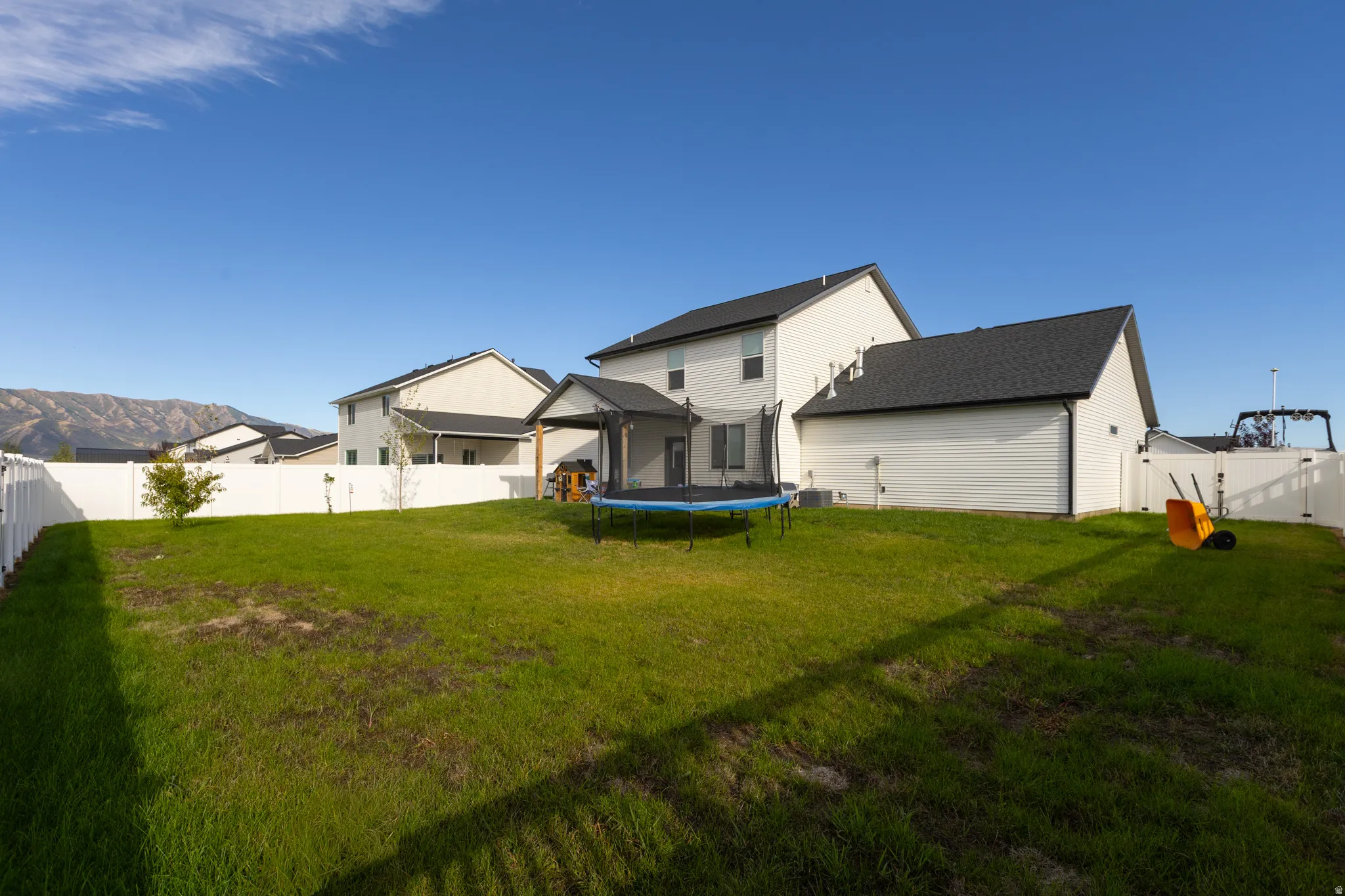 Expansive backyard with a manicured lawn, white vinyl fencing, and an integrated covered patio