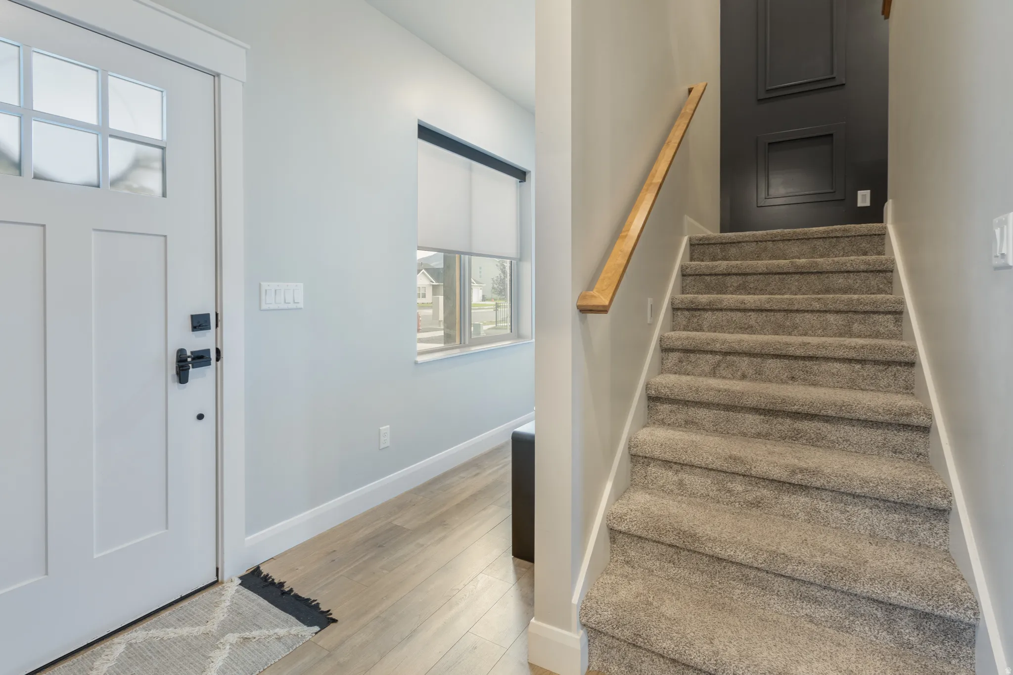 Entryway featuring a Craftsman-style door with decorative glass, wood-finish flooring, a window with a roller shade, and a carpeted staircase with a wood handrail