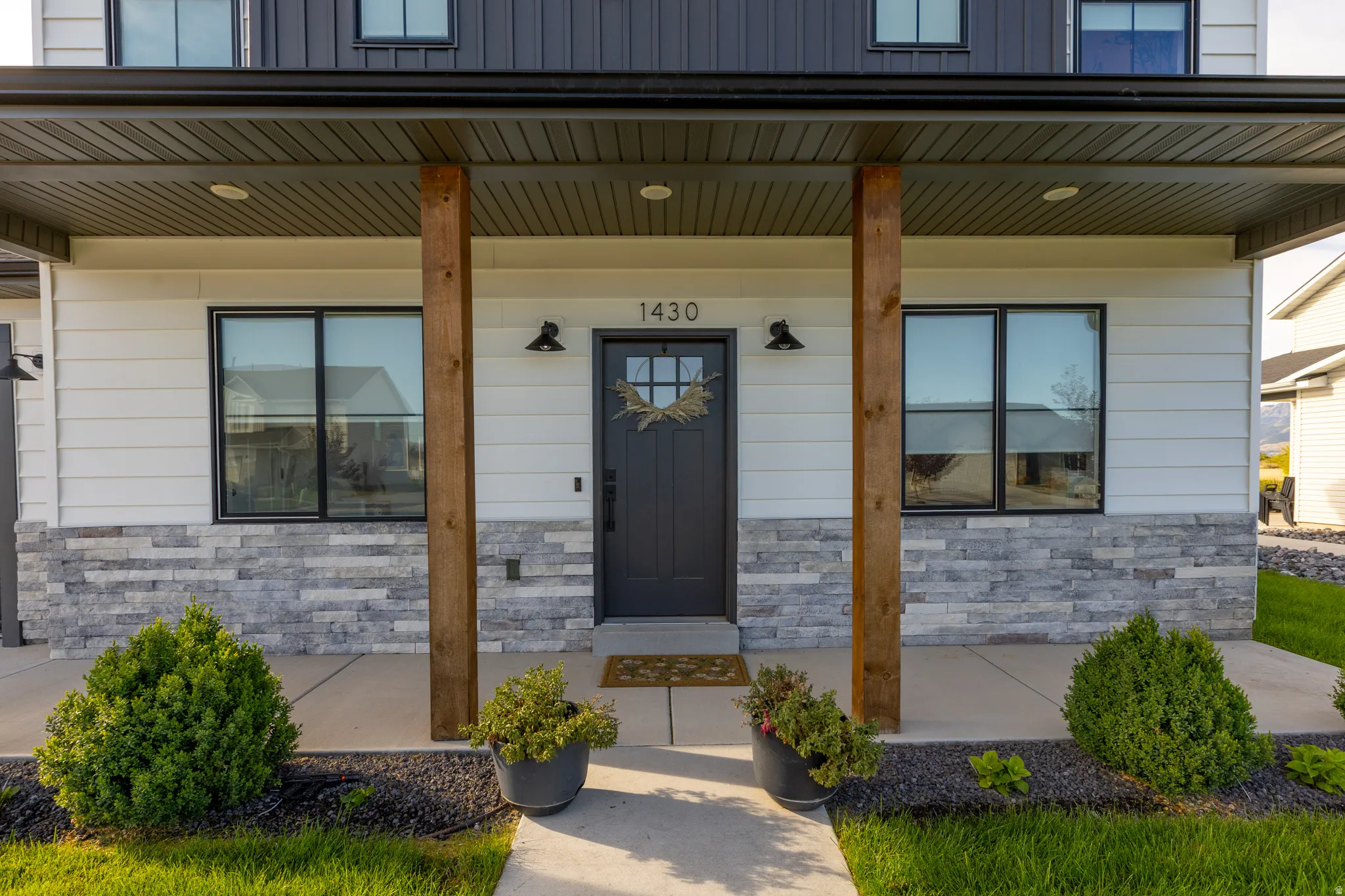 Covered entry with wood-wrapped columns, stone veneer accents, and white siding