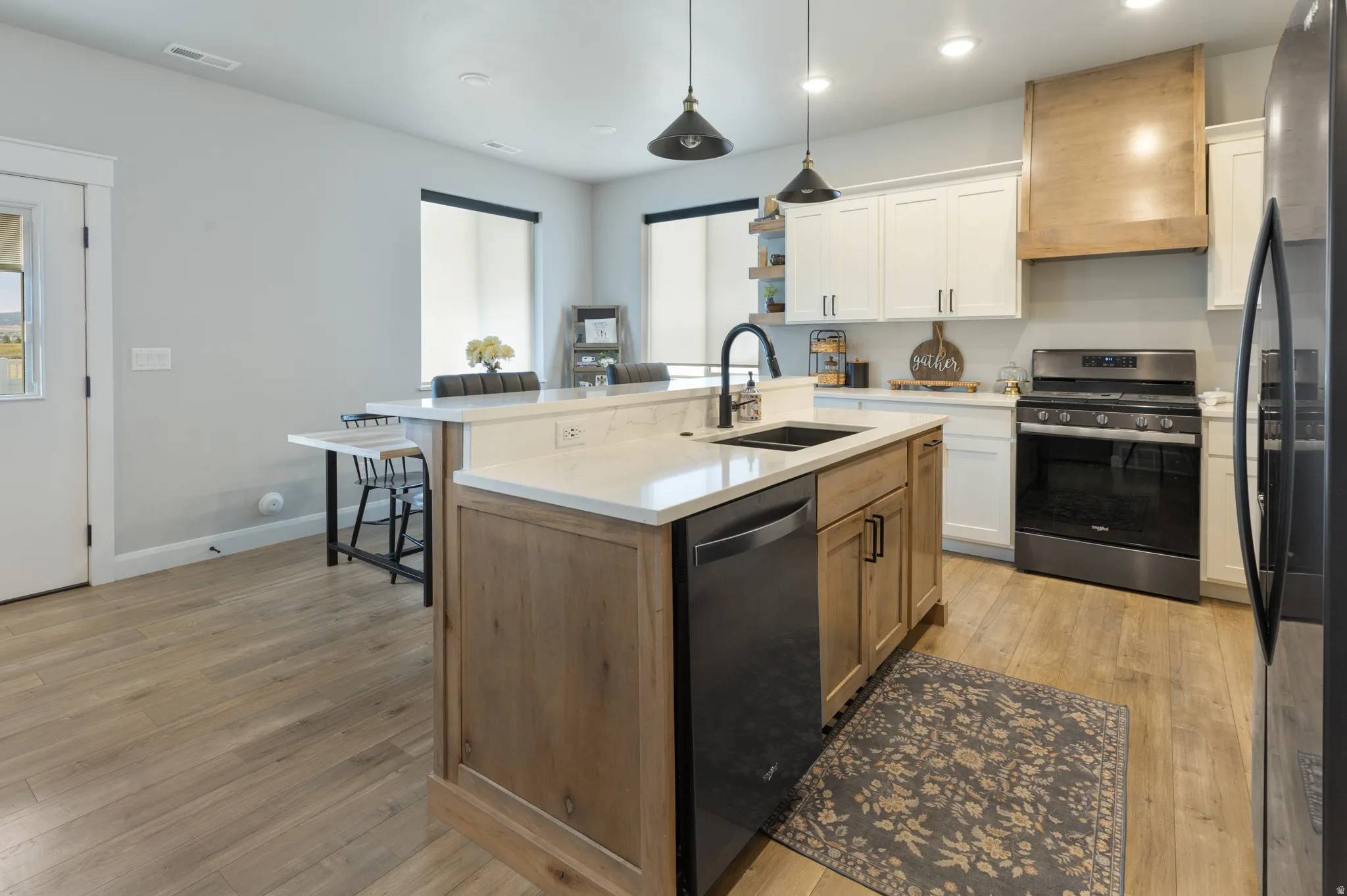 Kitchen featuring wood-finish flooring, two-tone cabinetry, stainless steel appliances, a center island with sink, and pendant lighting