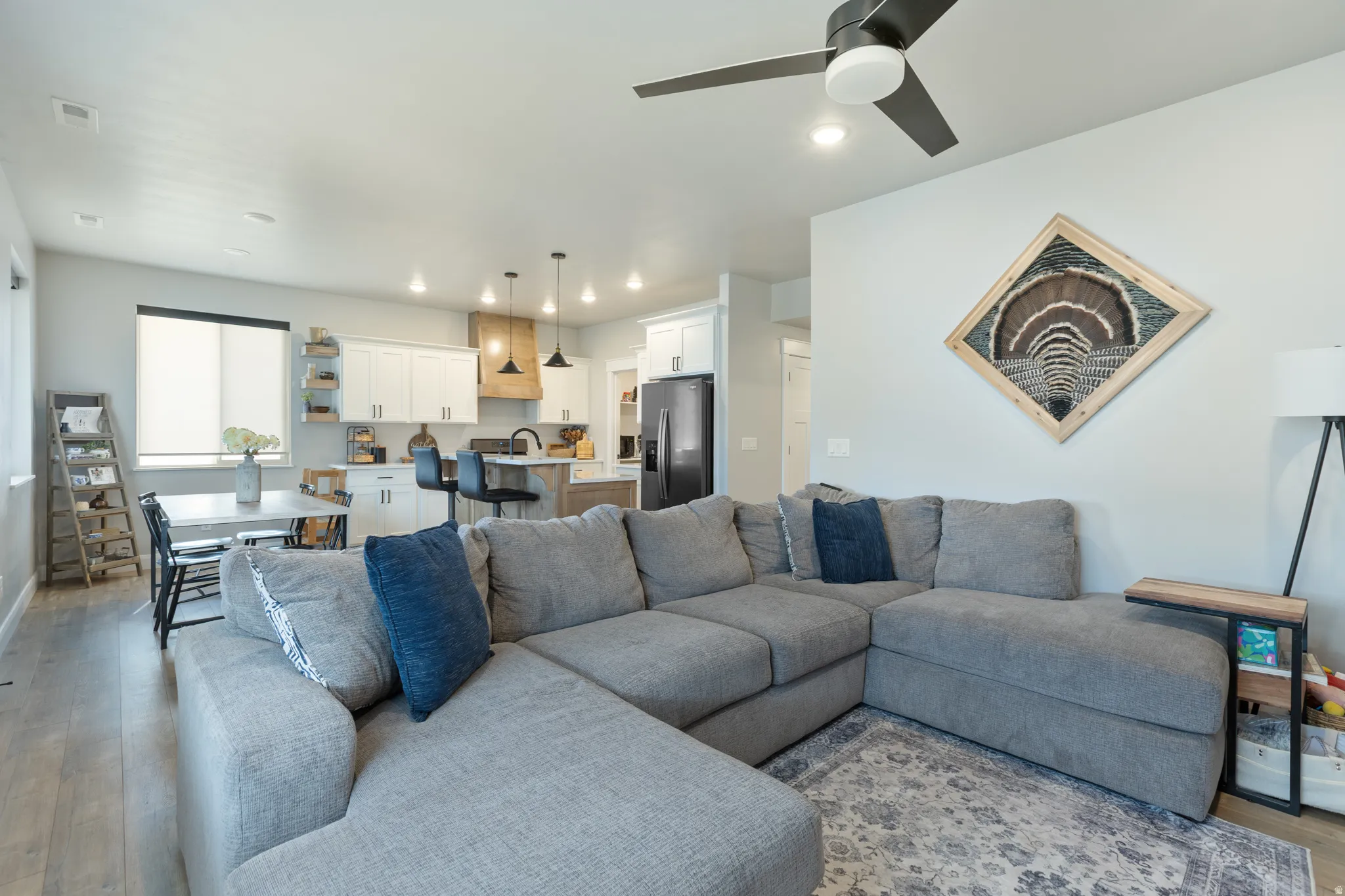 Open-concept living area featuring a spacious gray upholstered sectional sofa, wood-finish flooring throughout, and abundant natural light from multiple windows