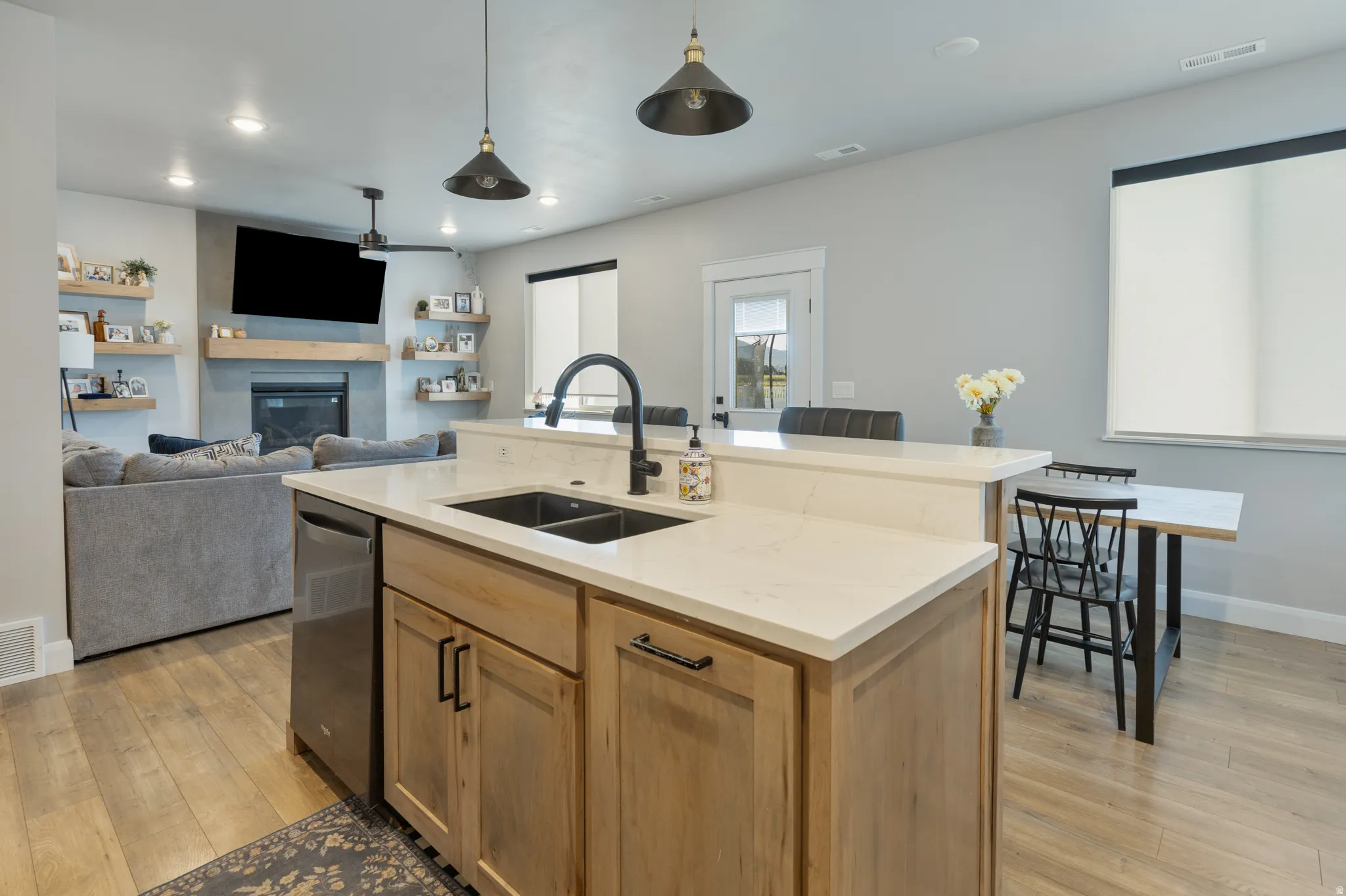 Kitchen island with light wood-finish cabinetry, light-toned countertops, and a double basin sink with a matte black faucet