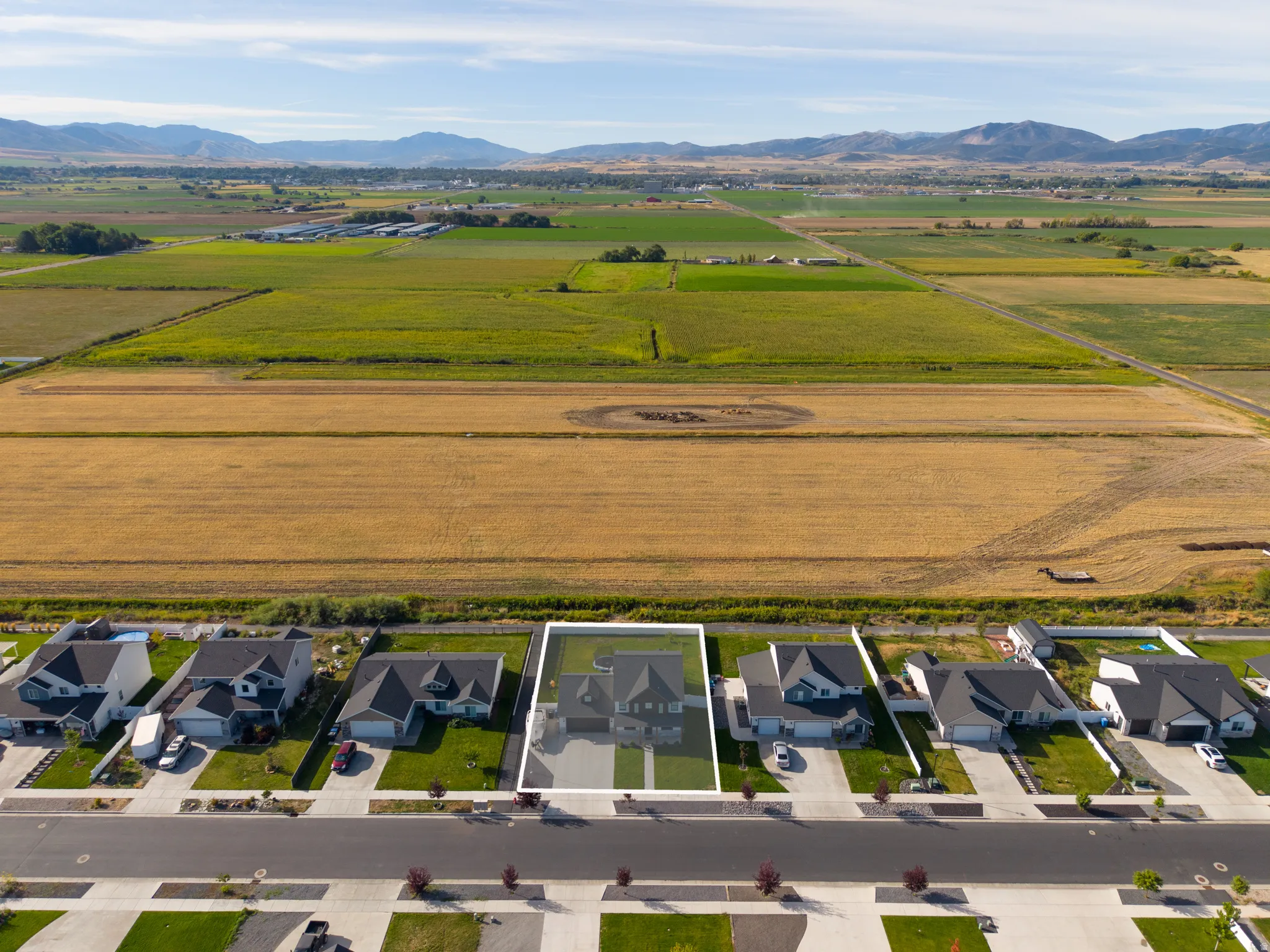 Aerial perspective showcasing the property's location within a residential street, bordered by agricultural fields and distant mountains