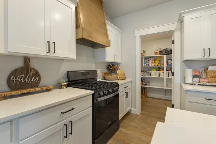 White cabinetry with matte black hardware, light-toned countertops, wood-finish flooring, a built-in gas range, and a walk-in pantry with shelving