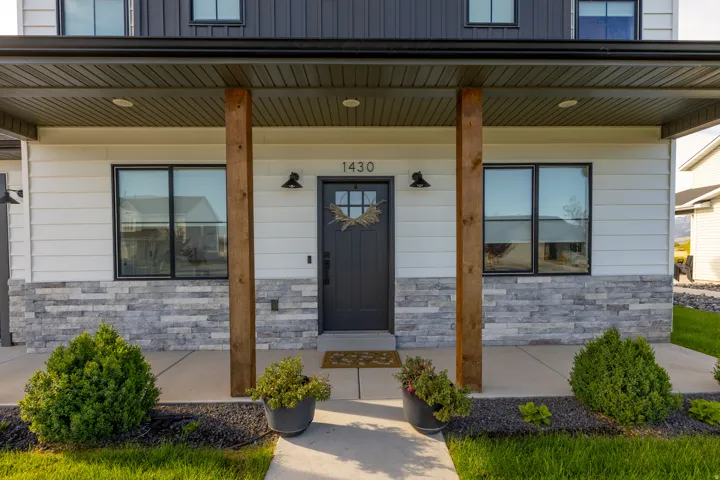 Covered entry with wood-wrapped columns, stone veneer accents, and white siding