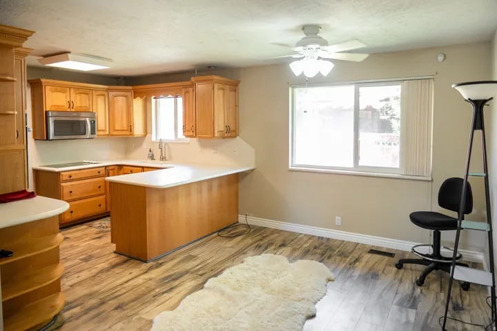 Kitchen featuring wood cabinetry, white countertops, stainless steel microwave, and wood-finish flooring