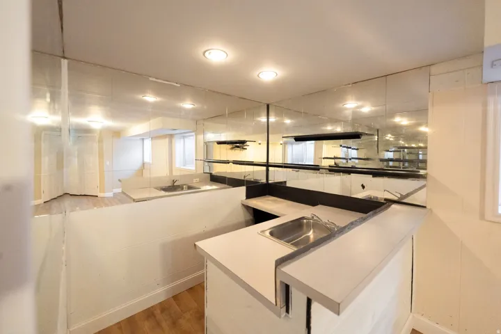 Built-in bar area featuring two stainless steel sinks, mirrored wall panels, overhead recessed lighting, and a window