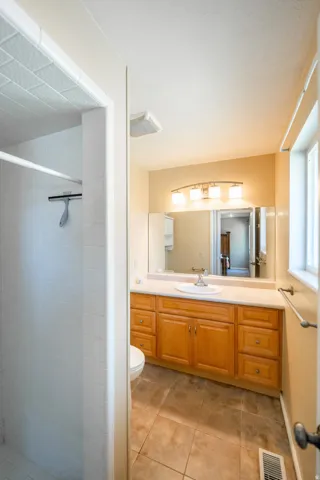 Bathroom featuring a single vanity with wood-finish cabinetry, a large mirror, a white sink, and tile flooring