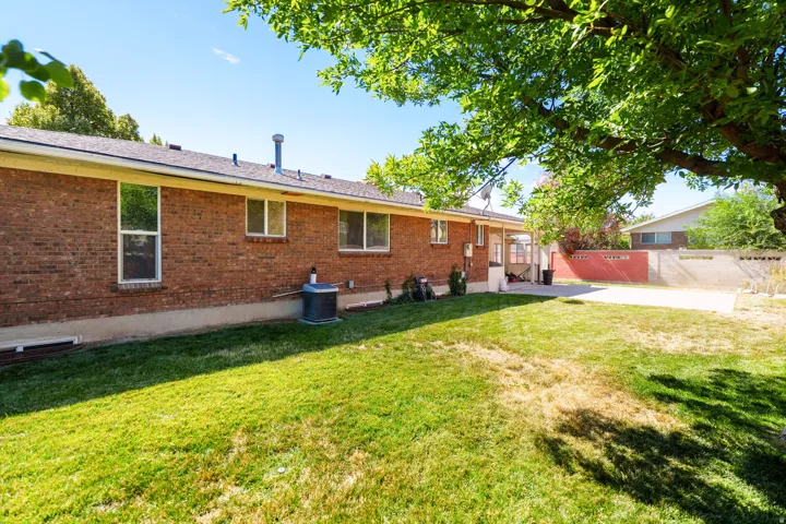 Brick exterior with multiple windows, a large grassy yard, and a concrete patio space