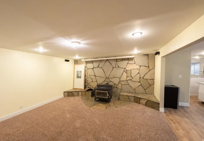 Stone-clad accent wall with a wood-burning stove, built-in hearth seating, recessed lighting, and carpeted flooring