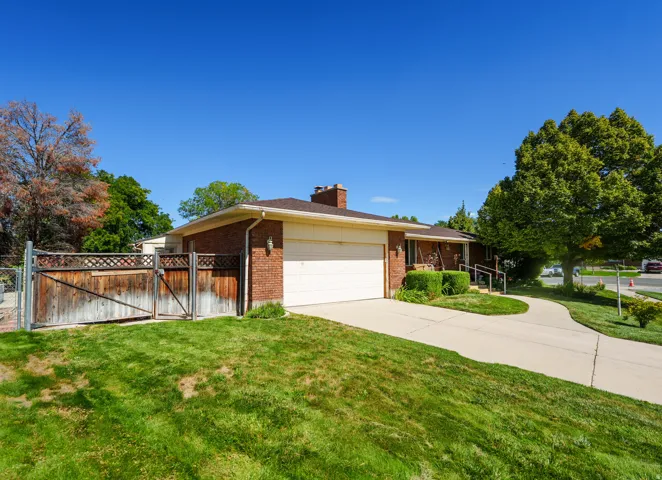 Brick exterior with an attached garage, paved driveway, and established trees