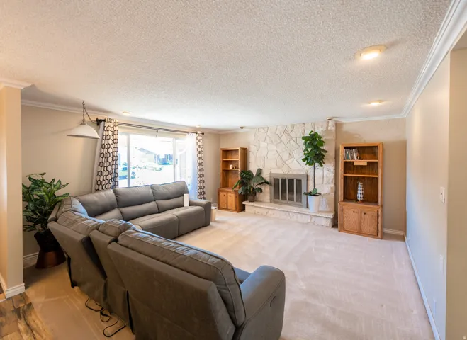Spacious living area featuring a stone fireplace, built-in shelving, crown molding, a sliding glass door, and recessed lighting