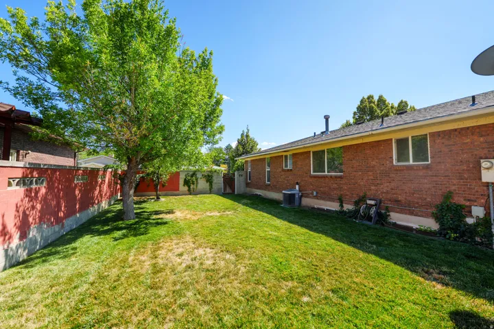 Expansive backyard featuring a mature tree, red brick wall, and a large green lawn