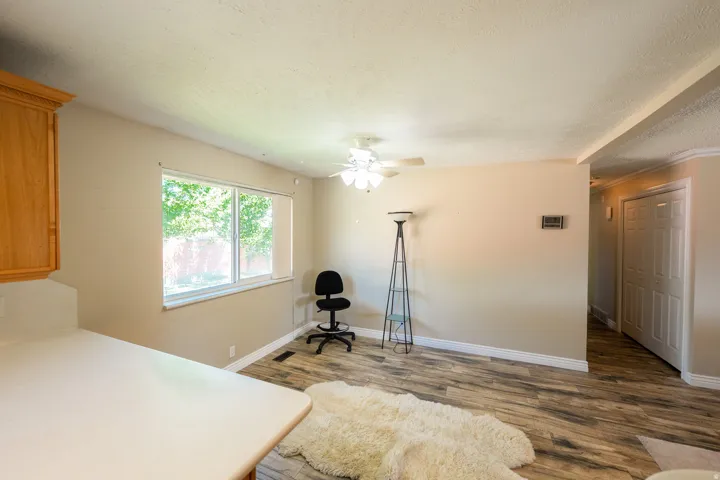 Wood-finish flooring throughout, light-toned walls, ceiling fan with integrated lighting, and a white six-panel door