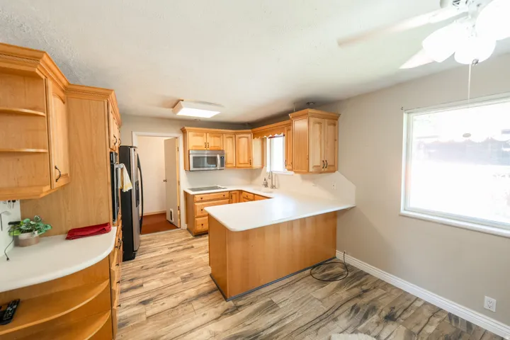 U-shaped kitchen featuring wood cabinetry, white countertops, wood-finish flooring, and stainless steel appliances