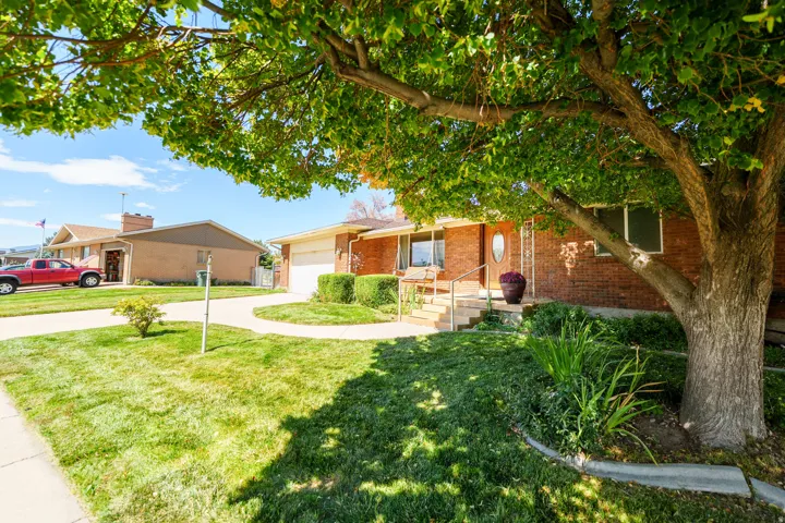 Brick exterior, front porch with railings, integral garage, established landscaping, and mature trees