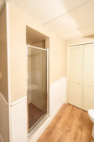 Glass-enclosed shower with tiled flooring, wood-finish flooring, and bi-fold louvered closet doors
