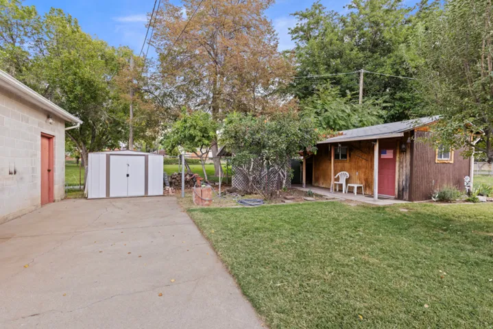 Expansive concrete patio with a storage shed, a separate building with wood-finish siding, and a grassy yard