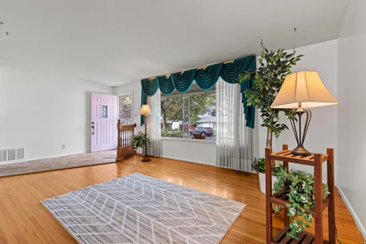Hardwood flooring throughout the room, large picture window, white painted walls, and wood railing
