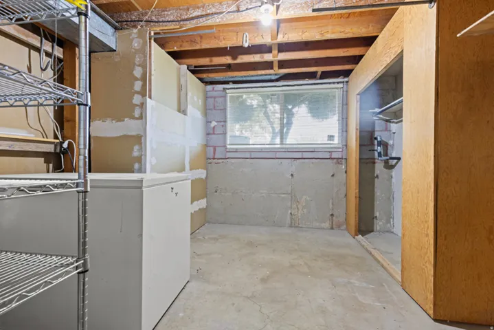 Basement with exposed wood ceiling beams, a window, concrete flooring, and partial wall framing