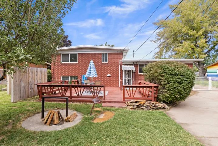 Red brick exterior with a wood deck, concrete fire pit, wood fence, and mature trees